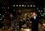 Produktionsbild aus ‚Jetzt oder nie‘ - Schauspieler Vincent Glander, im schwarzen Anzug, singt auf einer stimmungsvoll beleuchteten Bühne. Im Hintergrund ist die Band im Halbdunkel zu sehen.