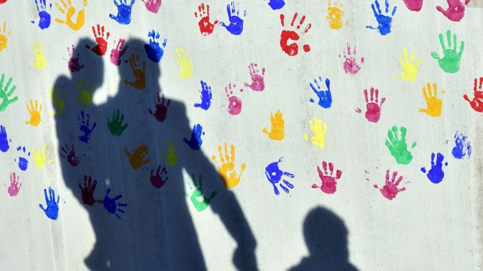 Soziales - München: Ein Mann mit einem Kind auf dem Arm und an der Hand wirft einen Schatten auf eine Wand einer Kita in München. Foto: Peter Kneffel/dpa/Archivbild