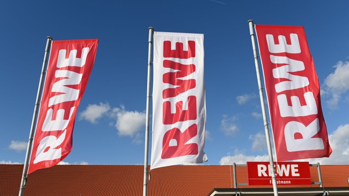 Einzelhandel - Düsseldorf: Fahnen mit dem Logo des Lebensmitteleinzelhändlers Rewe wehen vor einer Filiale. Foto: Uwe Zucchi/dpa/Archivbild