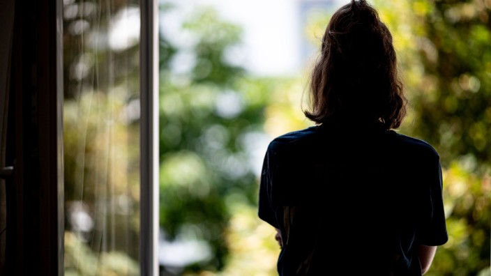 Gesundheit - Potsdam: Eine junge Frau steht in ihrer Wohnung am Fenster. Foto: Fabian Sommer/dpa/Illustration