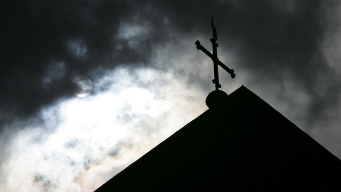 Kirche - Berlin: Im Gegenlicht und vor wolkenverhangenem Himmel ist die Kirchturmspitze des Doms mit Kreuz zu sehen. Foto: Friso Gentsch/dpa/Symbolbild