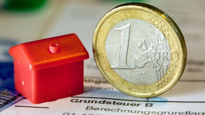 Finanzen - Magdeburg: Eine Münze und ein Spielzeughaus stehen auf einem Abgabenbescheid für die Entrichtung der Grundsteuer. Foto: Jens Büttner/ZB/dpa/Illustration