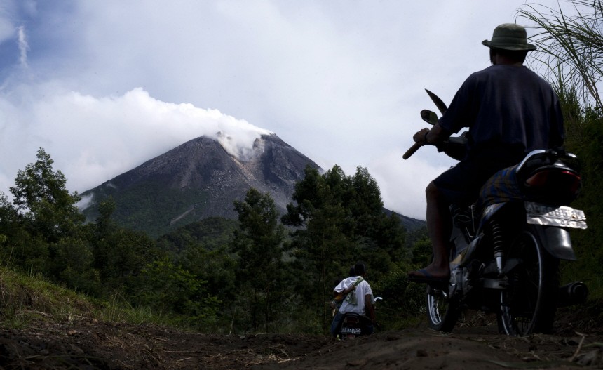 Villagers ride in motorcycles while Mount Merapi volcano emitting smoke is seen from Cangkringan village