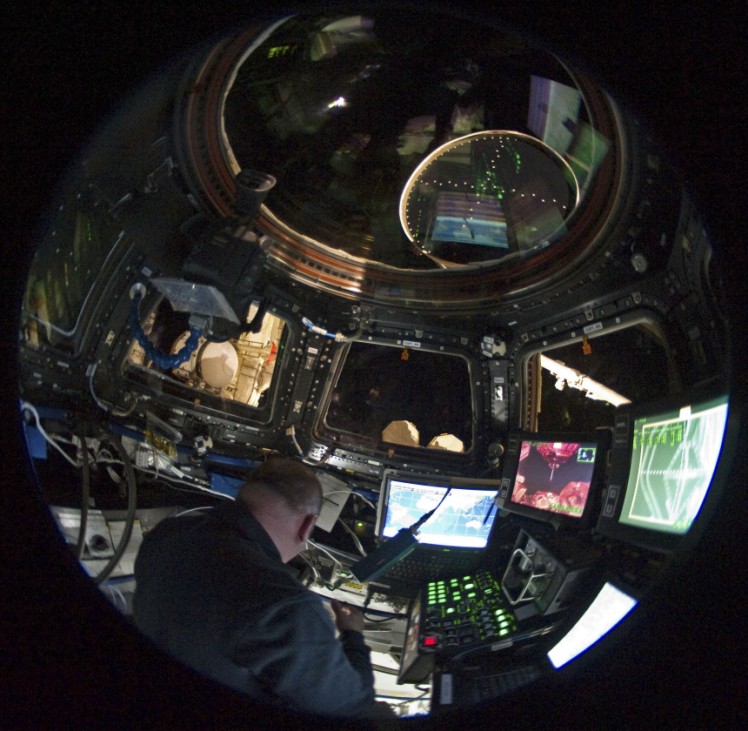 In this circular fish-eye lens view, NASA astronaut Garrett Reisman, is surrounded by windows and computers inside the International Space Station's Cupola.