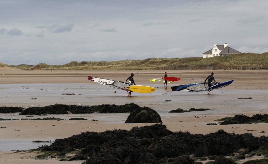 Windsurfers carry their boards along Rhosneigr beach on Anglesey