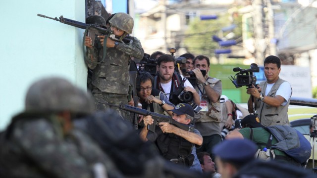 Army soldiers, police and journalists take their positions during an operation by the authorities at Alemao slum in Rio de Janeiro