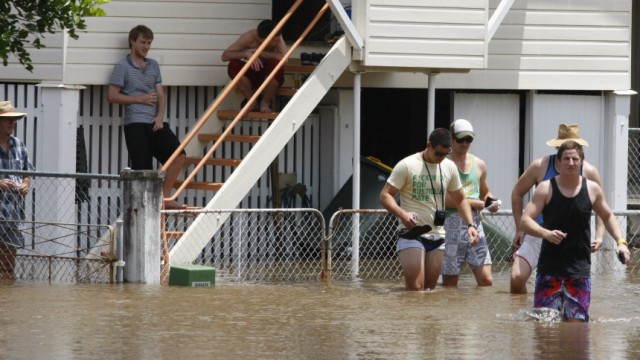 Teenagers wade through a flooded street in the Brisbane suburb of Breakfast Creek