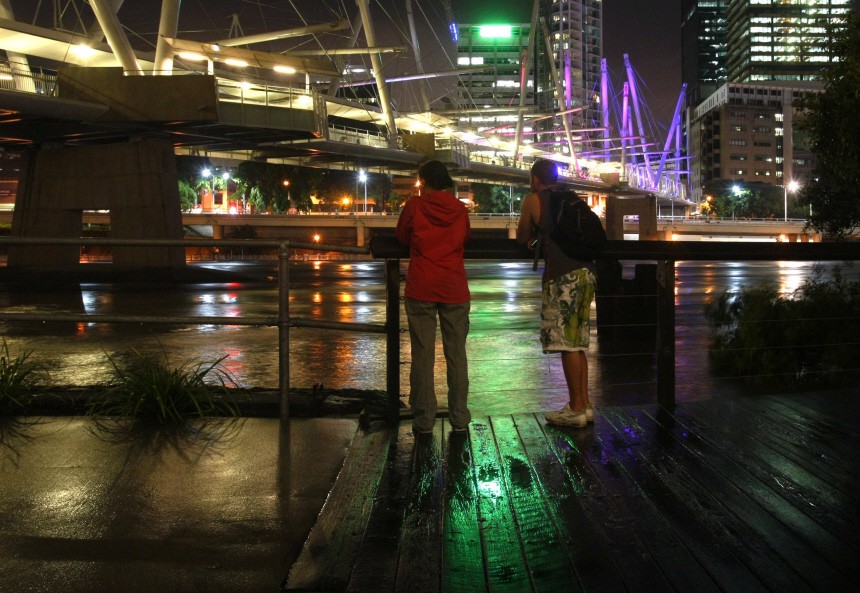 Residents look on near the Kurilpa Bridge as the Brisbane River flows past central Brisbane