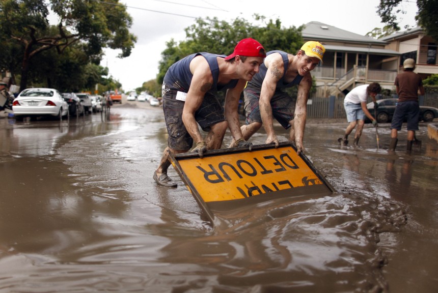 Men use a road sign to push mud off a road after floodwaters receded in the Brisbane suburb of Westend