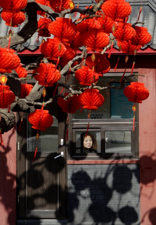 A woman looks out of a window next to a tree with decorative red lanterns ahead of the Chinese Lunar New Year celebrations in Beijing