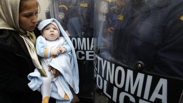 An Afghan asylum seeker holding a child stands in front of riot policemen during a demonstration in Athens