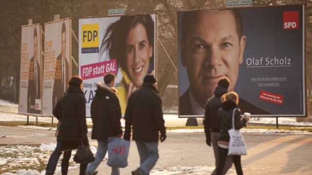 People walk past election campaign placards showing top candidates of CDU, FDP and SPD for upcoming Hamburg state elections in Hamburg