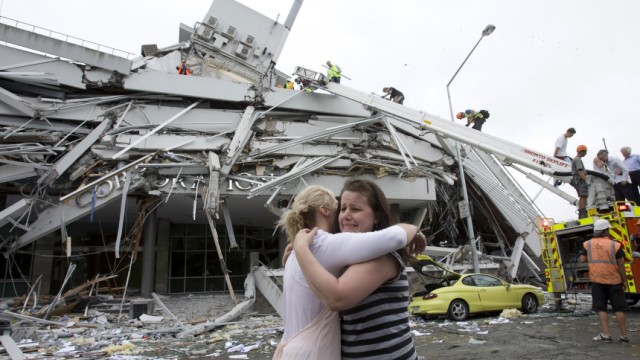 Two women hug each other in front of a collapsed building in central Christchurch