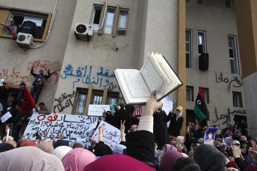 An anti-government protester holds the Muslim holy book, the Koran, while protesters chant anti-government slogans in Benghazi city