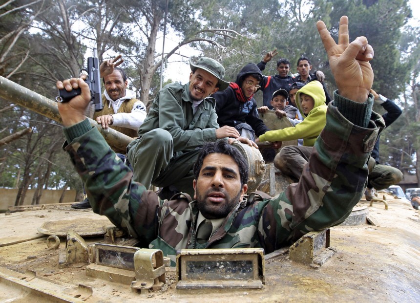 A man fires his pistol into the air as he celebrates with other people in an army armoured vehicle in Shahat