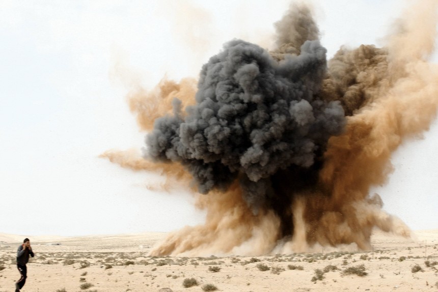 A rebel holds his ears as a bomb launched by a Libyan air force jet loyal to Libya's leader Muammar Gaddafi explodes in the desert near Brega