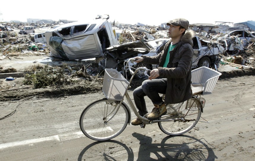 A resident rides a bicycle beside damaged vehicles among debris after the earthquake and tsunami in Sendai