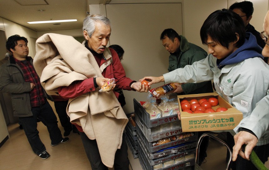 An evacuee receives food from government officers in an aisle at an evacuation centre in Sendai
