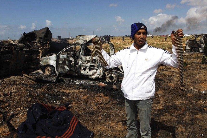 A Libyan youth stands beside the charred body of a Gaddafi loyalist soldier on the outskirts of Benghazi