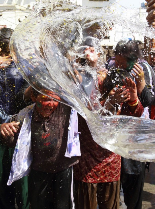 People react after getting splashed by a bucket of water while celebrating the festival of Holi in Kathmandu