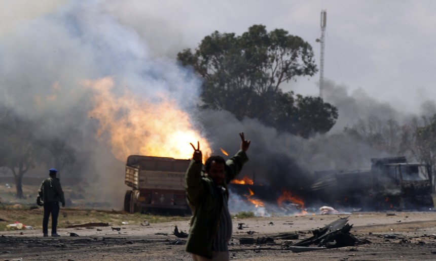 Rebel fighter gestures in front of burning vehicles belonging to forces loyal to Libyan leader Gaddafi after air strike by coalition forces along road between Benghazi and Ajdabiyah