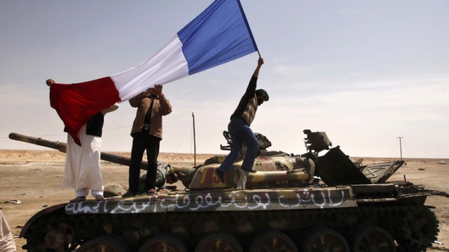 A man waves a French flag on top of a destroyed tank belonging to forces loyal to Libyan leader Muammar Gaddafi in Ajdabiyah