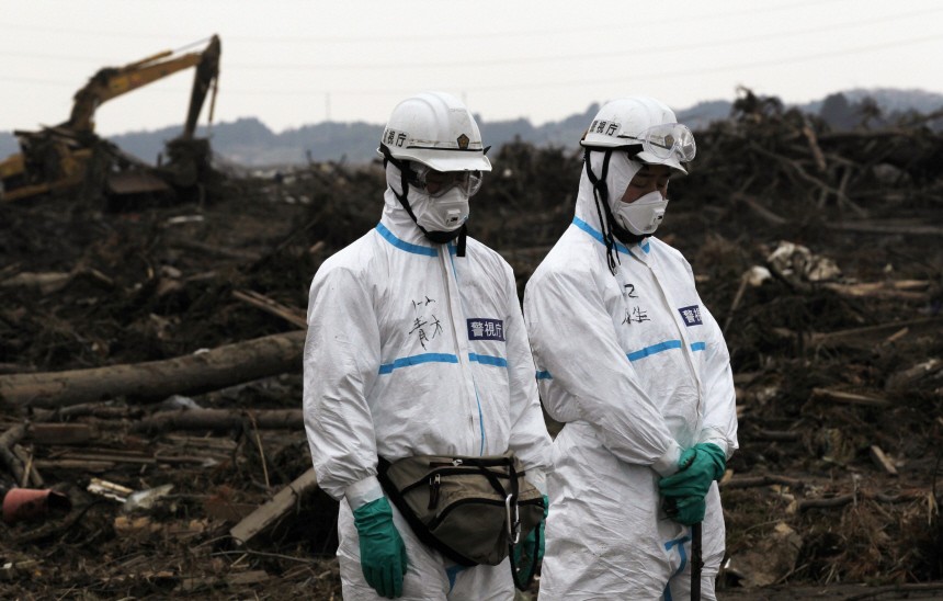 Police officers in protective suits observe a moment of silence for those who were killed by the March 11 earthquake and tsunami, as they search for bodies at a destroyed area in Minamisoma, Fukushima prefecture