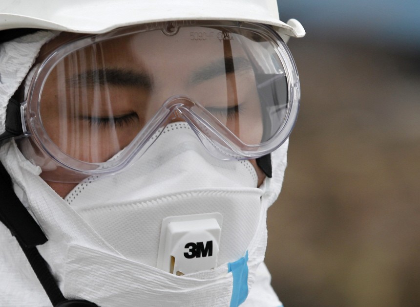 A police officer in a protective suit observes a moment of silence for those who were killed by the March 11 earthquake and tsunami, as they search for bodies at a destroyed area in Minamisoma, Fukushima prefecture