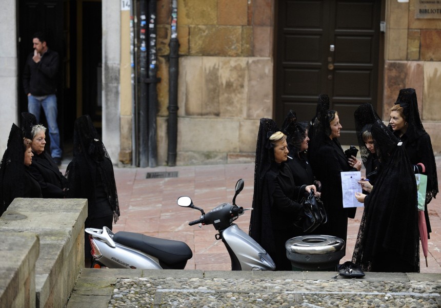 Women wearing traditional mantilla dresses smoke before the start of the procession of the 'Silencio y la Santa Cruz' brotherhood during Holy Week in Oviedo