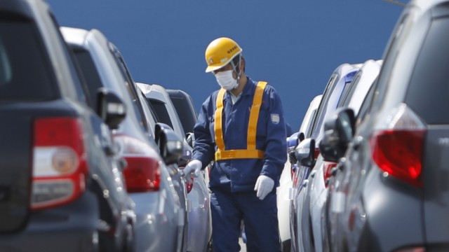 Worker walks among newly produced Toyota cars to drive to a cargo ship at Sendai port in Sendai