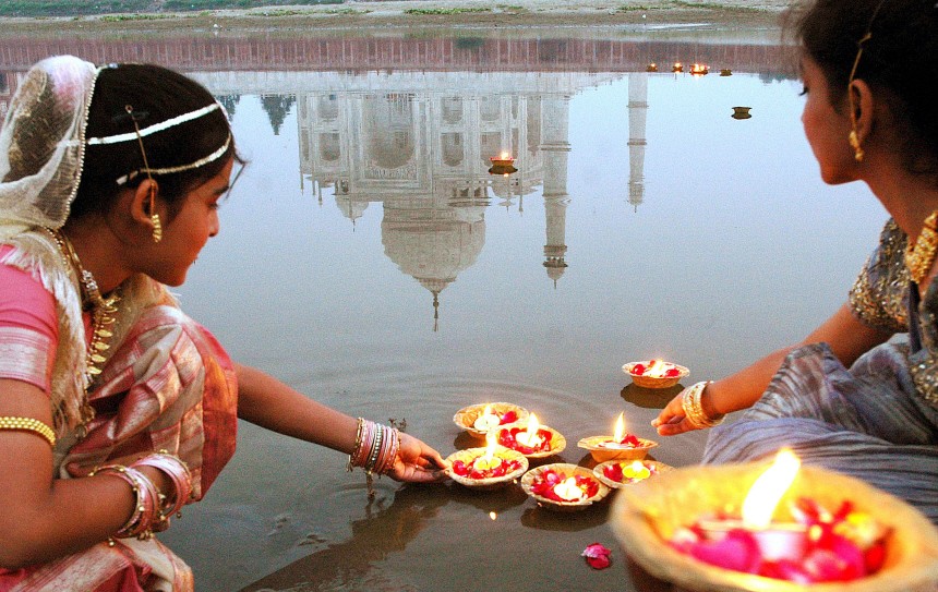 Indian teenagers place oil lamps onto the Yamuna River behind the Taj Mahal