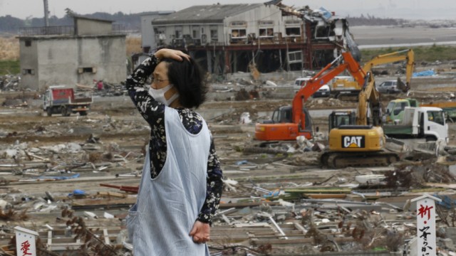 A woman reacts as she looks around a devastated area by March 11th's earthquake and tsunami in Natori
