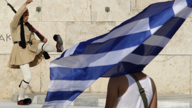 A protester holds a Greek flag as a Greek Presidential guard marches at the monument of the unknown soldier in Athens