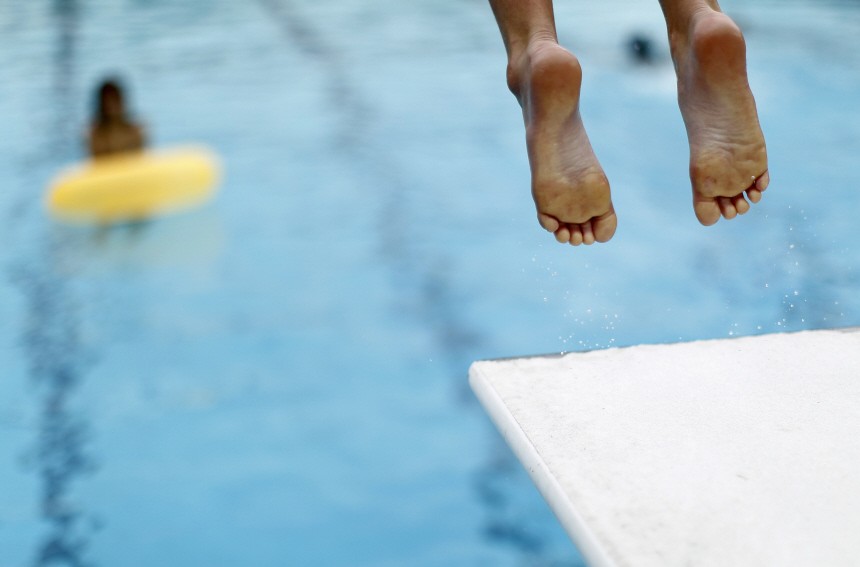A boy jumps off a diving board into a swimming pool to cool off, in Solana Beach