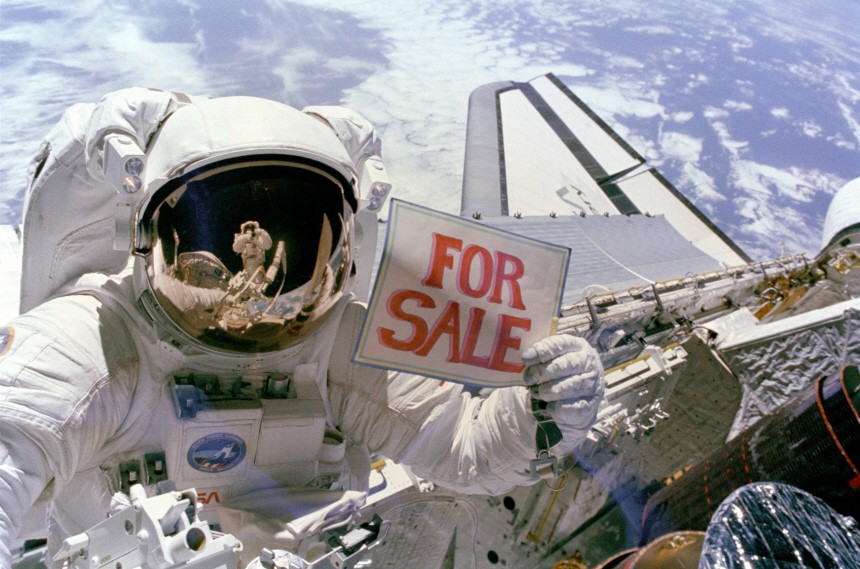 NASA handout photo of astronaut Dale Gardner holding a For Sale sign aboard the Space Shuttle Discovery