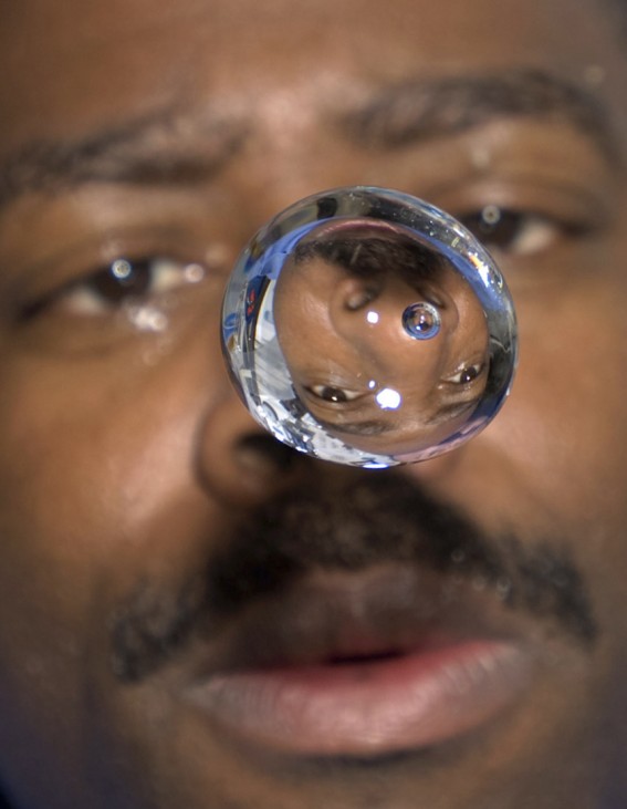 Astronaut Melvin watches water bubble float between him and camera, showing his image refracted, on middeck of space shuttle Atlantis