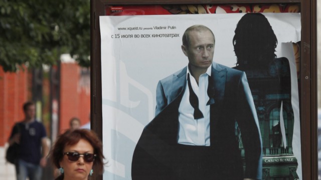 People walk past an advertising hoarding overlaid with a poster of Russia's Prime Minister Vladimir Putin posing as a secret agent in Moscow