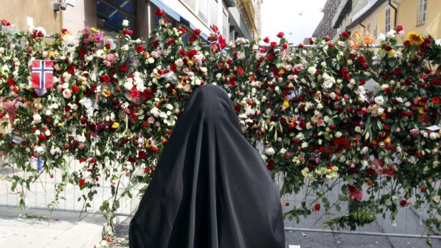 A Muslim woman stands in front of a sea of floral tributes placed outside the Oslo Cathedral