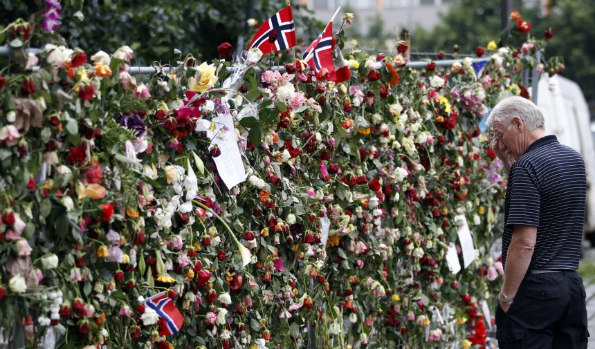 A man stands in front of a fence with flowers near the destroyed government building's area in Oslo