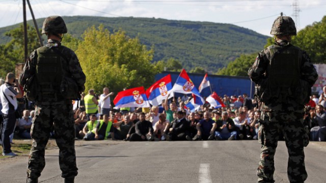 Kosovo Serbs wave flags while sitting on the road in front of Slovenia's KFOR soldiers in Rudare near  Zvecan