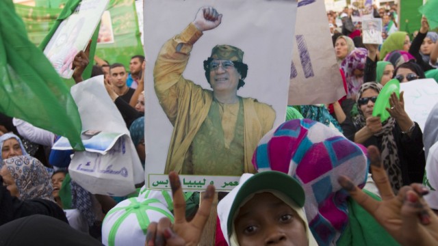 A woman gestures near a picture of Libyan leader Muammar Gaddafi during a pro-government rally in Tripoli