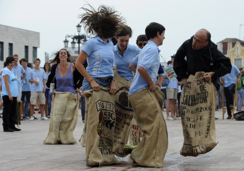 A monk joins a group of French pilgrims in a sack race in Oviedo