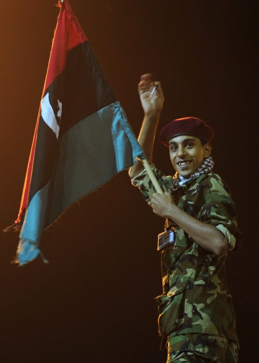 A Libyan gestures while holding a Kingdom of Libya flag as people gather near the courthouse in Benghazi