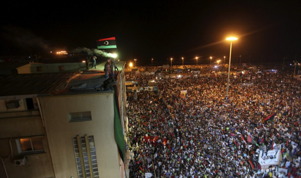 A Kingdom of Libya flag is held aloft a building as people gather near the courthouse in Benghazi
