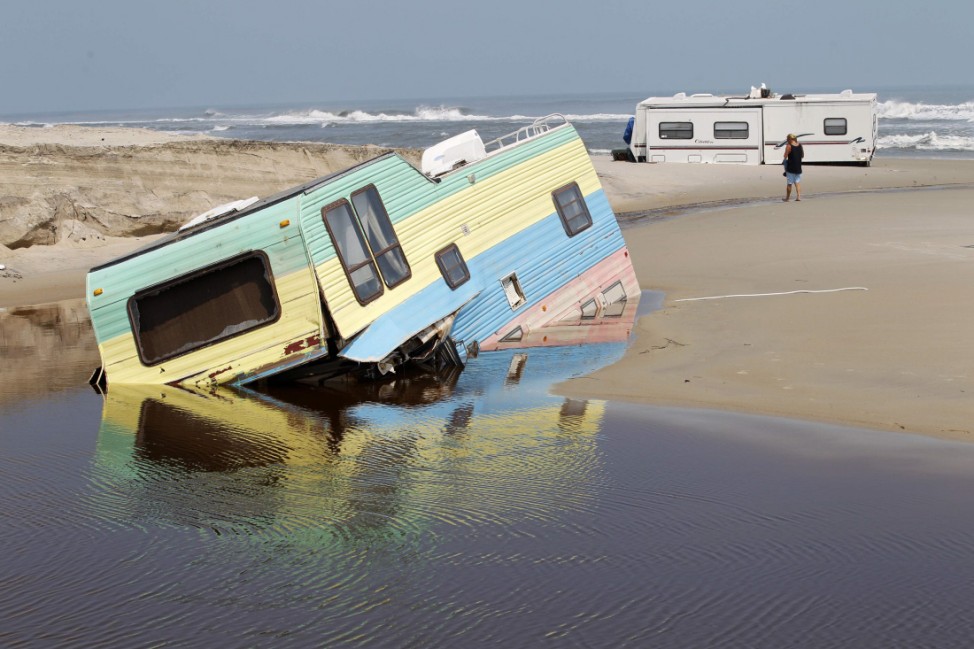 Residents walk past a trailer as it lies on the beach after being washed out by Hurricane Irene at Cape Hatteras National Seashore in Rodanthe