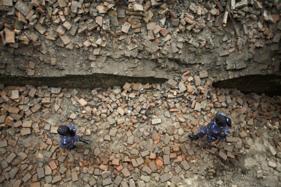 Nepalese police walk on a street filled with bricks from quake-damaged houses in Bhaktapur