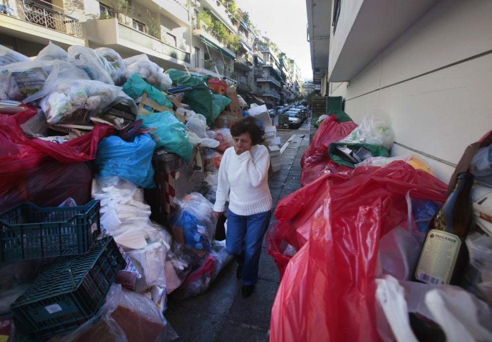 A woman covers her nose as she walks by a wall of pilling garbage during a strike by municipality workers and garbage collectors in Athens
