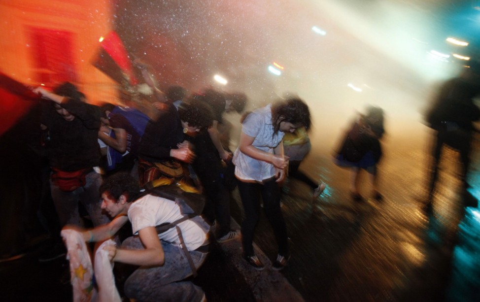 Demonstrators are hit by a jet of water released from a riot police vehicle during a protest in Santiag