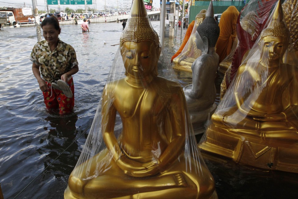 A woman walks next to Buddha statues at a flooded area at Pathum Thani province