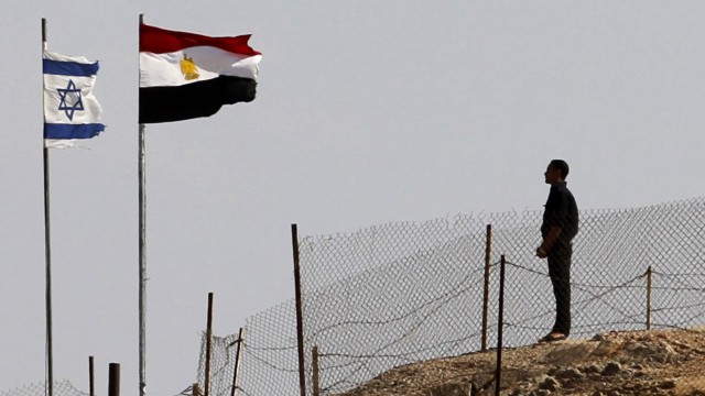 An Egyptian soldier stands near the Egyptian national flag and the Israeli flag at the Taba crossing between Egypt and Israel